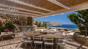An outdoor dining area with a stone wall, a round table, and chairs. - Rocky Mansion Mykonos (Mykonos)