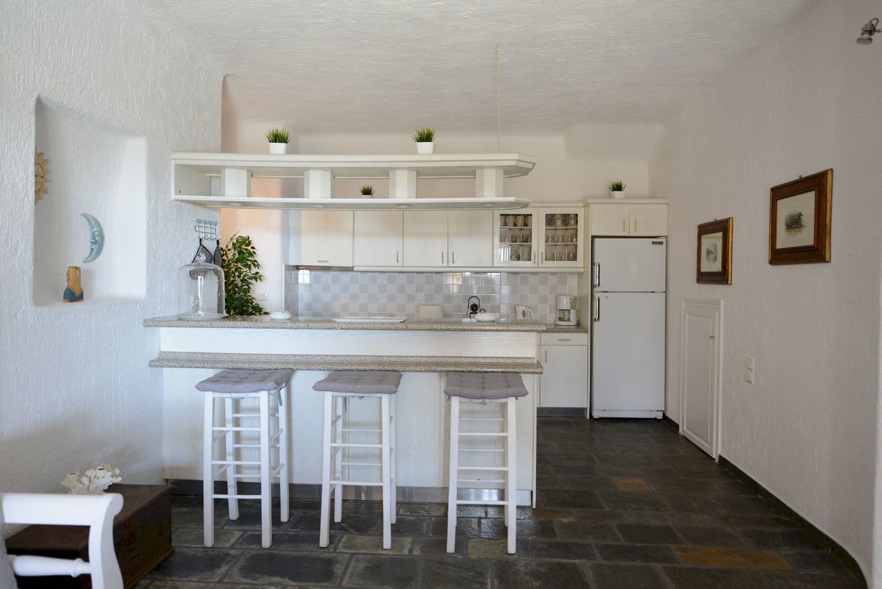 Una cocina moderna con armarios blancos, una isla central con taburetes, un refrigerador y un microondas.