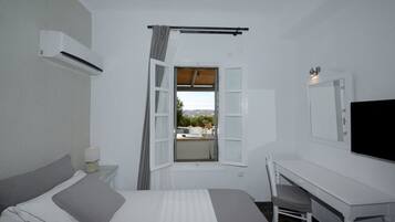 Un dormitorio con cama, escritorio, silla, ventana con cortinas, televisor montado y aire acondicionado.