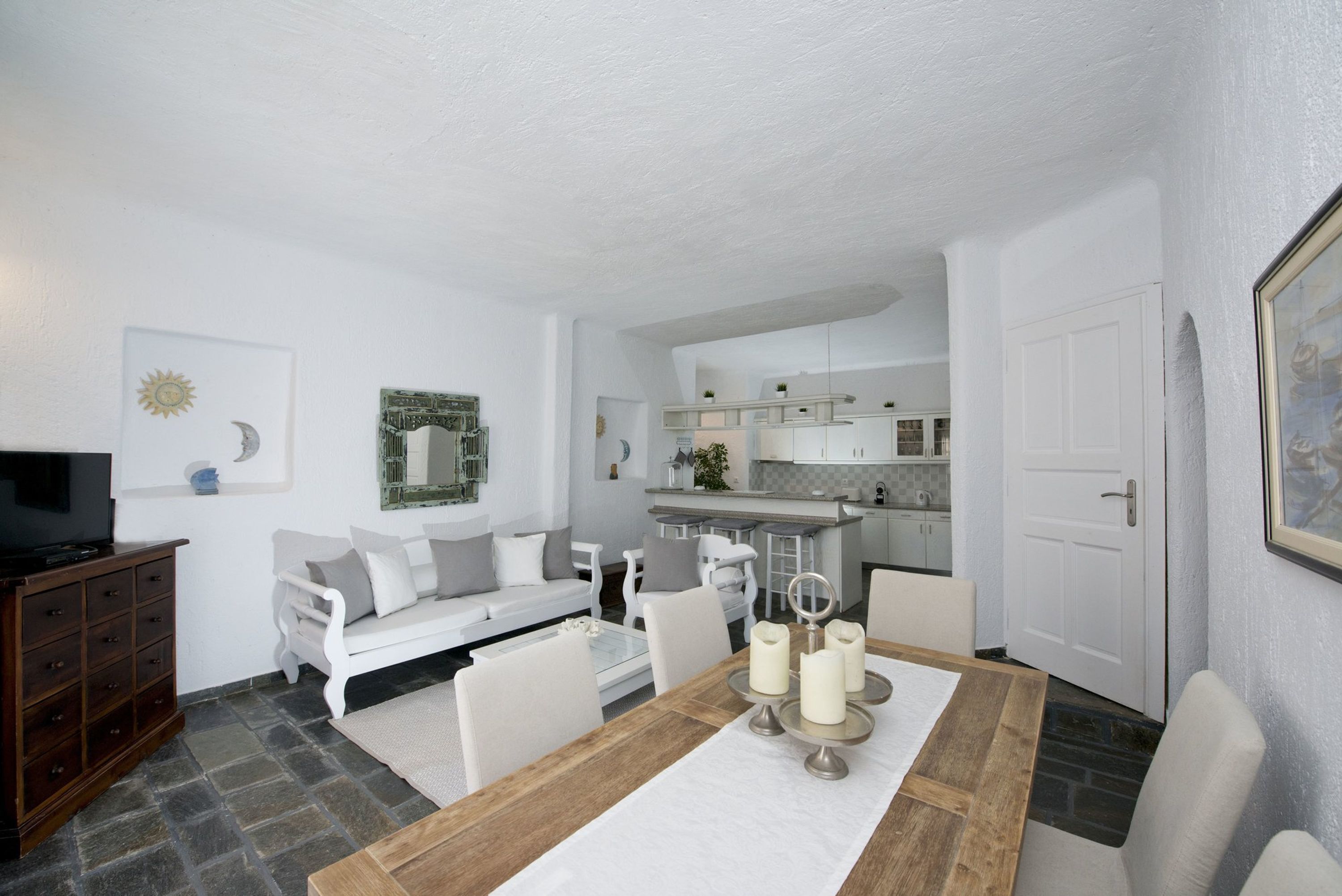 Una sala moderna con comedor, muebles blancos y una cocina al fondo.