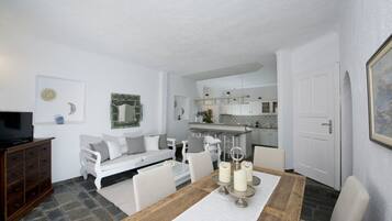 Una sala moderna con comedor, muebles blancos y una cocina al fondo.