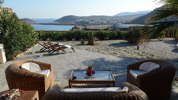 Un patio con mobiliario de mimbre, una mesa de vidrio y vistas al mar y colinas.