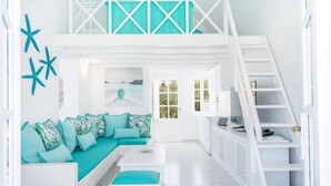 A bright, white interior with a teal sofa, a white staircase, and a view through a door.