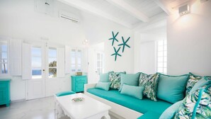 A bright, white interior with a teal sofa and matching cushions, a white coffee table, and teal accent pieces.