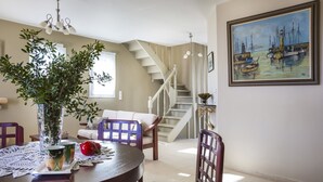 Un comedor con una mesa redonda, sillas, un jarrón con plantas y un cuadro en la pared.