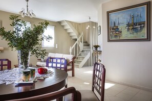 A dining area with a round table, chairs, a vase with plants, and a painting on the wall. - Villa Serenity sleeps 9! (Matsoukata)