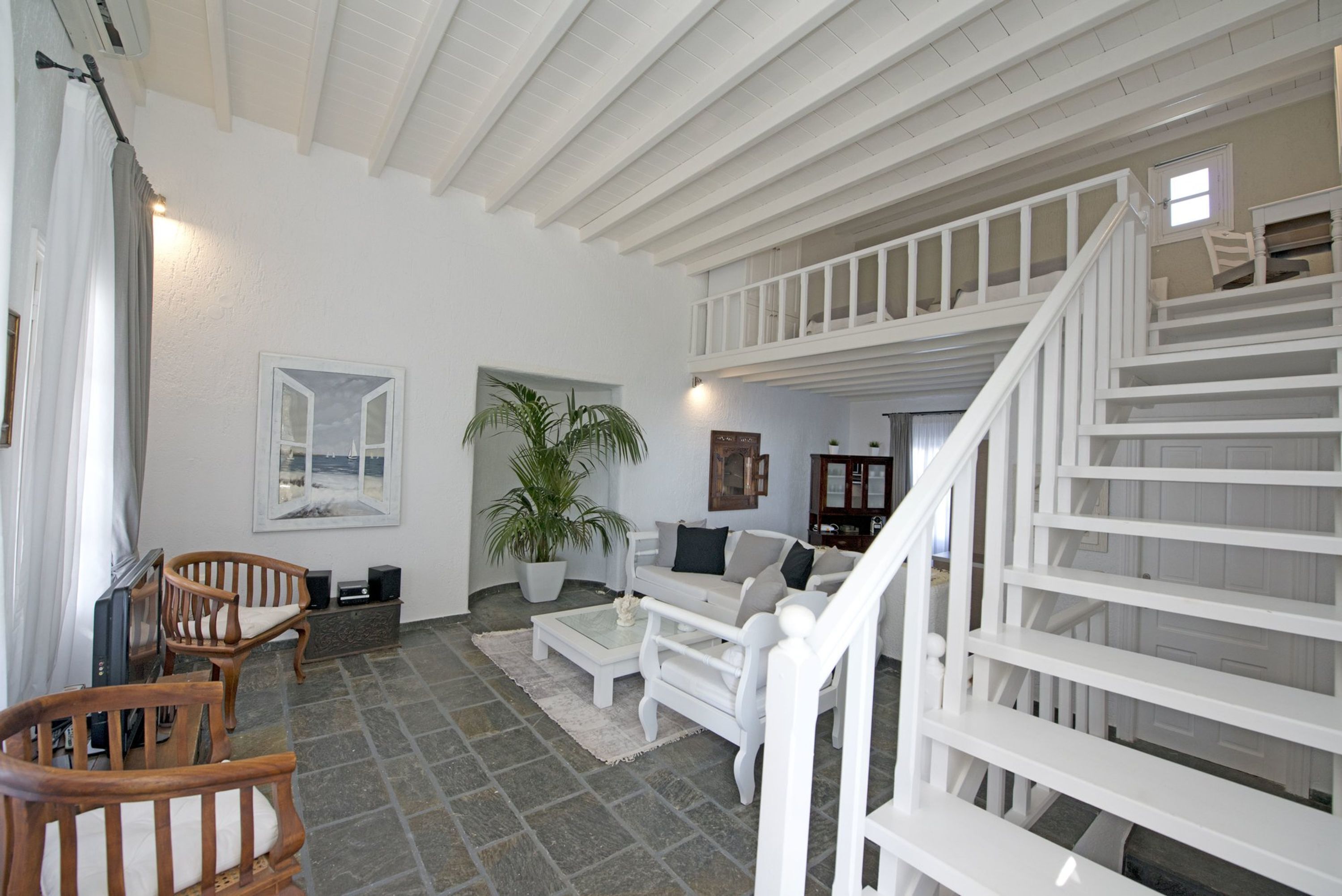 Amplia sala de estar con una escalera blanca, muebles de madera y una planta grande en maceta.