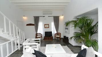Una sala de estar con un sofá blanco, una mesa de centro, un televisor y una planta grande.