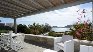 Un patio al aire libre con mobiliario blanco, suelo de piedra y vistas al mar y las colinas.