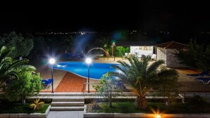 A nighttime view of a swimming pool area with a curved design, surrounded by palm trees and lounge chairs.
