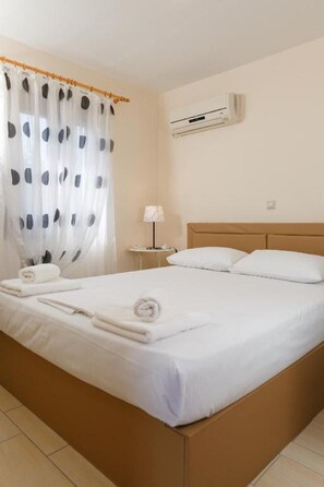 A neatly made bed with white linens and towels, a bedside lamp, and an air conditioning unit on the wall. - Glyfada    Villas II (Paralio Astros)