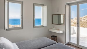 Een slaapkamer met twee bedden, een raam met uitzicht op zee, een spiegel en een klein plankje met een beker en een kaars.