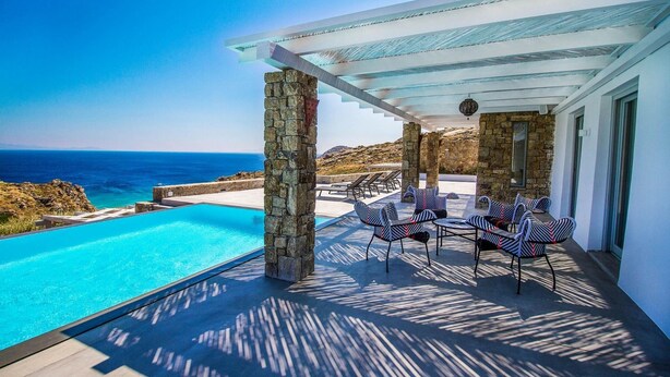 Ein Poolbereich mit Blick auf das Meer, Steinpfeilern und Gartenmöbeln.