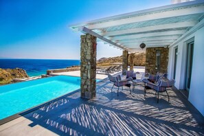 A poolside area with a view of the sea, stone pillars, and outdoor seating. - Artemis | 7BD minimal villa, Private pool, Jacuzzi (Mykonos)