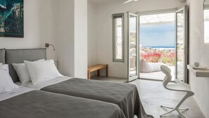 Ein Hotelzimmer mit zwei Betten, einer Bank, einem weißen Stuhl und einem großen Fenster mit Blick auf das Meer und rote Blumen.