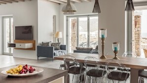 Ein modernes Wohnzimmer mit einem Holzespeisetisch, transparenten Stühlen, einem an der Wand befestigten Fernseher und einer durch das Fenster sichtbaren Steinwand.