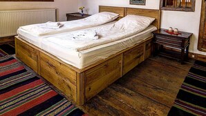 Una cama de madera con ropa blanca, una mesita de noche pequeña, un radiador y una ventana con cortina.