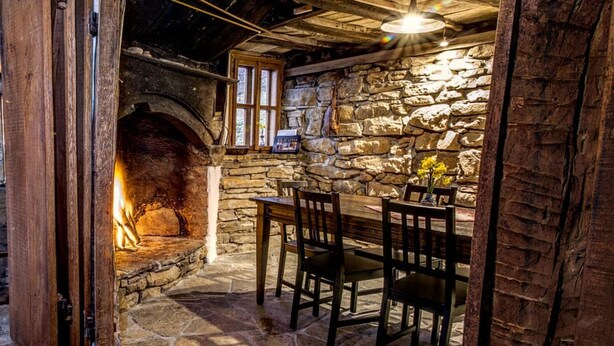 Un interior rústico con chimenea de piedra, vigas de madera y una pared de piedra.