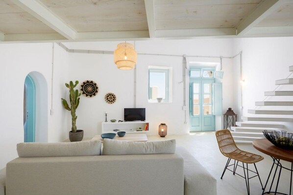 Ein modernes Wohnzimmer mit einer Couch, einem Esstisch, einem Fernseher und einer Treppe.