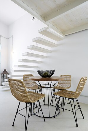Un comedor moderno con una mesa de madera y cuatro sillas de mimbre, estructura de metal negro y una escalera blanca al fondo.