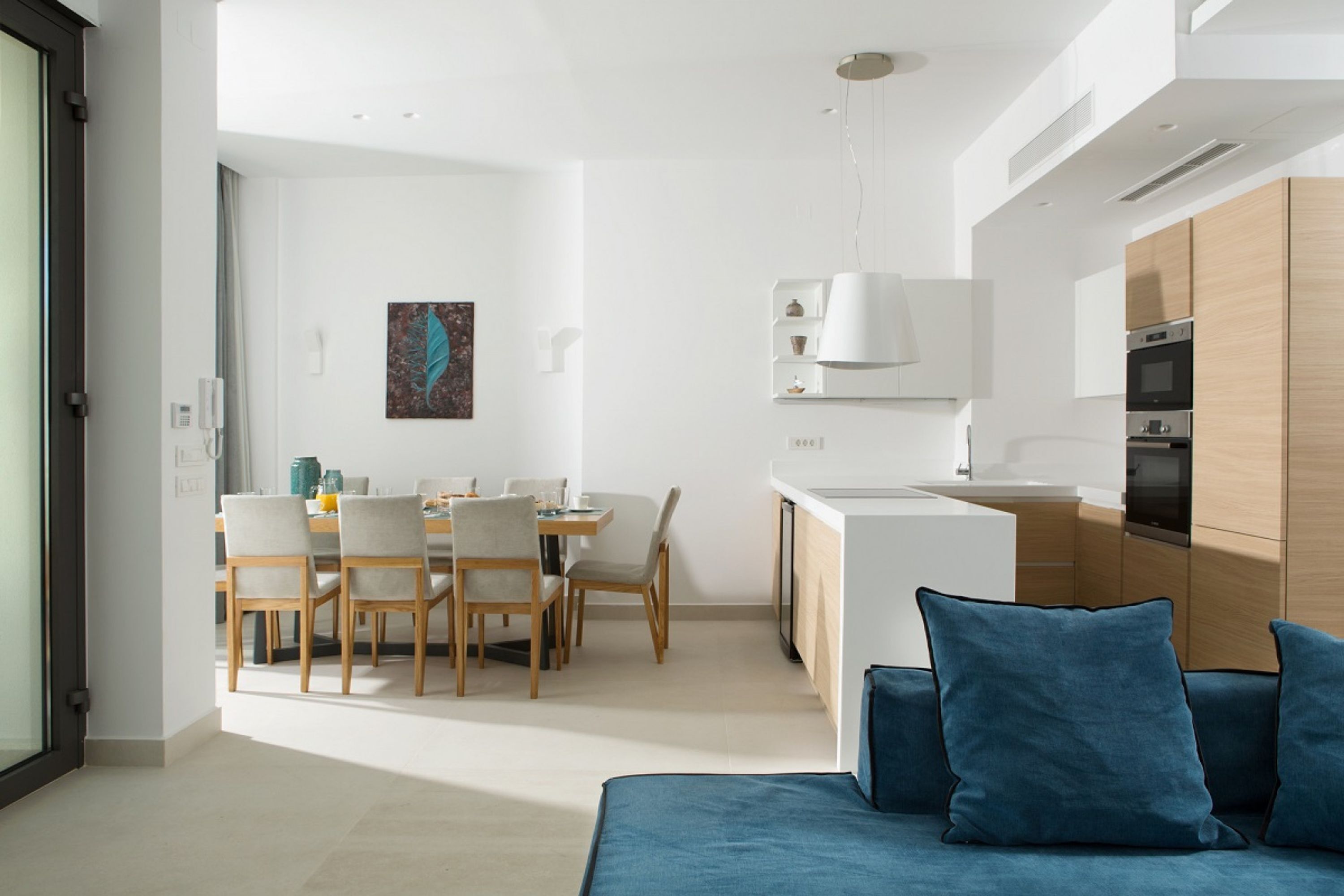 Un espace de vie moderne et bien éclairé, comprenant un canapé, une table à manger avec des chaises et une cuisine dotée de meubles en bois et d’appareils électroménagers.