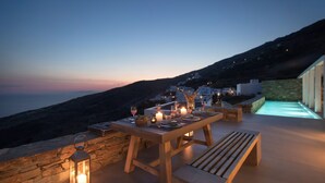 Un espacio exterior para comer con una mesa dispuesta para dos, un banco y un muro de piedra.