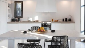 Una cocina moderna con armarios blancos, encimera de mármol y una zona de comedor con sillas negras.