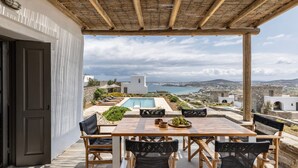 An outdoor dining area with a wooden table and chairs, overlooking a pool and a scenic view of the sea and hills. - Sky 3 Bedroom Villa Sea View Private Pool (Kolympithres)