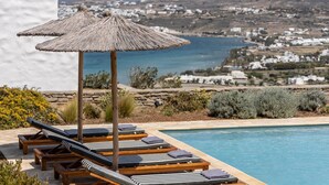 A poolside area with wooden loungers and a straw umbrella, overlooking a coastal town. - Sky 3 Bedroom Villa Sea View Private Pool (Kolympithres)