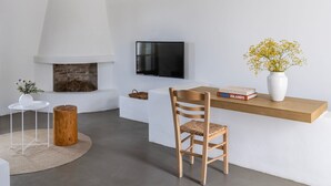 Ein modernes Wohnzimmer mit Kamin, einem an der Wand montierten Fernseher, einem Holzstuhl, einem weißen Tisch und einem Regal mit Büchern und einem Blumenstrauß.