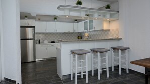 A compact kitchen with white cabinets, a built-in island with bar stools, a stainless steel refrigerator, and a tiled backsplash. - Villa Fragkia/private lounge area, sea view (Kalafatis)