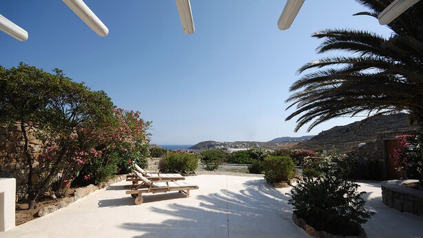 A sunlit patio with lounge chairs, a stone wall, and a view of the sea and hills. - Villa Fragkia/private lounge area, sea view (Kalafatis)