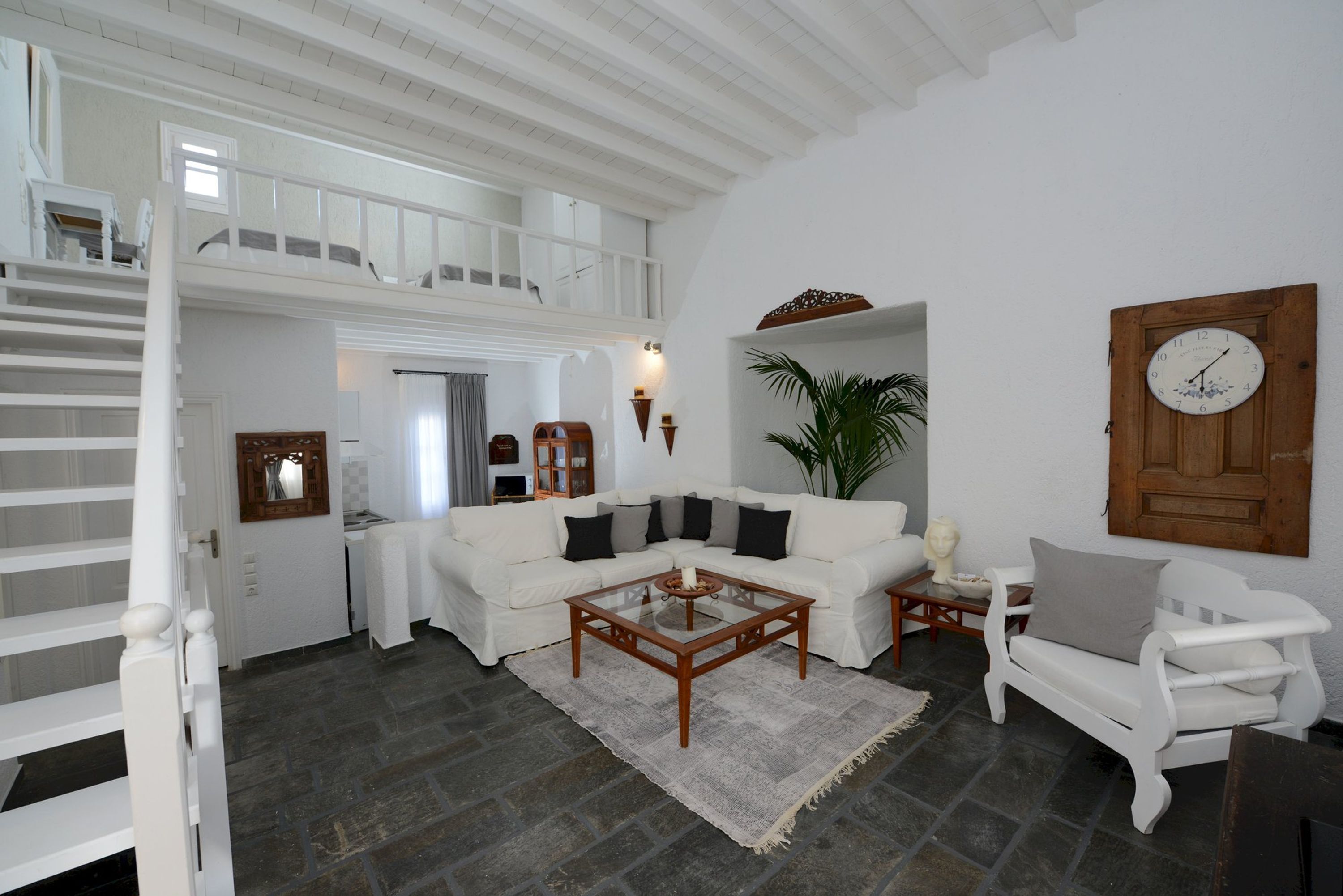 Un amplio espacio de estar con un sofá blanco, una mesa de centro y una silla de madera. Una escalera conduce a un nivel superior.