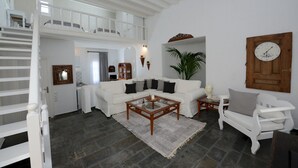 A spacious living area with a white sofa, a coffee table, and a wooden chair. A staircase leads to an upper level. - Villa Fragkia/private lounge area, sea view (Kalafatis)