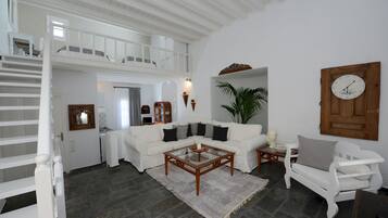 Un amplio espacio de estar con un sofá blanco, una mesa de centro y una silla de madera. Una escalera conduce a un nivel superior.