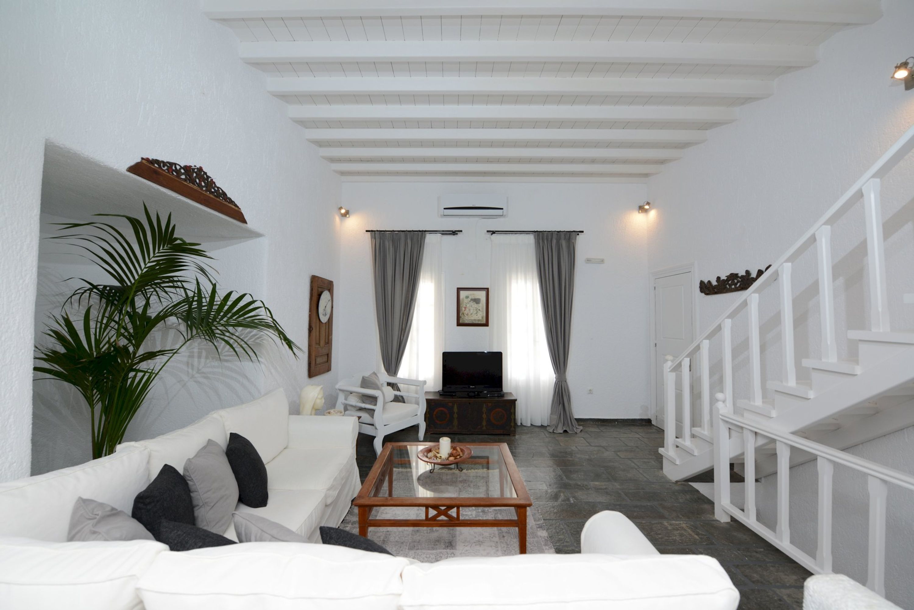 Una sala de estar con un sofá blanco, una mesa de centro, un televisor y una escalera.