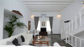 Una sala de estar con un sofá blanco, una mesa de centro, un televisor y una escalera.