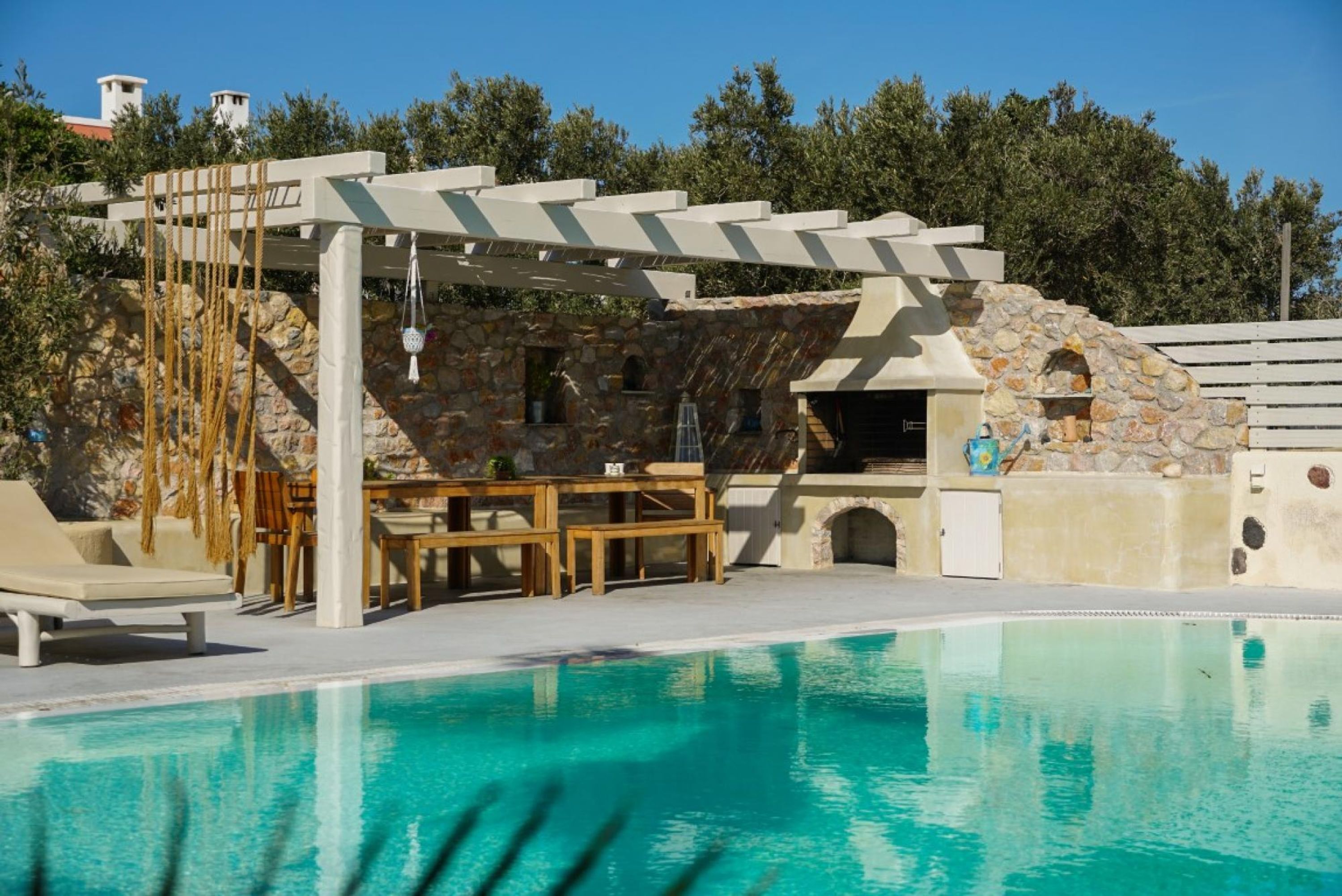Un espace piscine agrémenté d’une pergola, d’un mur en pierre et de coins salon extérieurs.