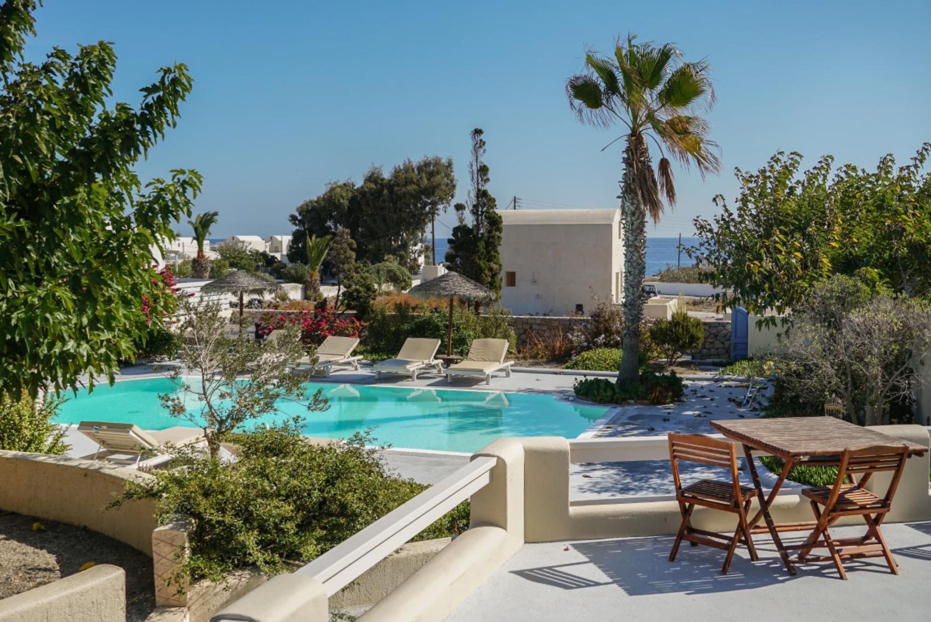 A pool area with lounge chairs and a table, surrounded by greenery and buildings.