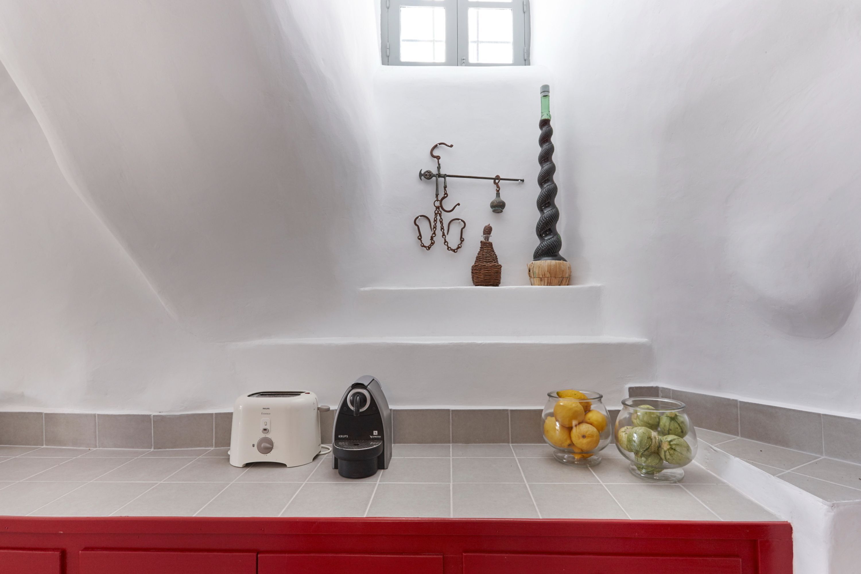 Cozinha com bancada branca, armário vermelho, torradeira, cafeteira e dois potes de vidro com limões e limas.