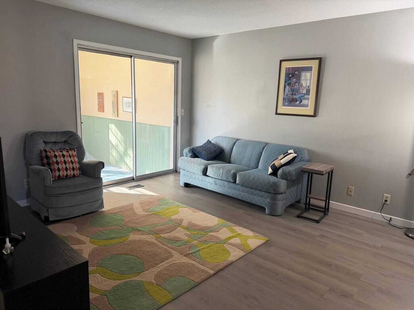 Un salon avec un fauteuil gris, un canapé bleu, un tapis à motifs et un tableau encadré au mur.