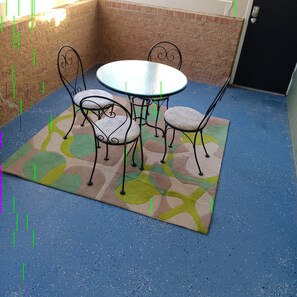 Eine Terrasse mit rundem Tisch, vier Stühlen, einem gemusterten Teppich und einer Backsteinmauer.