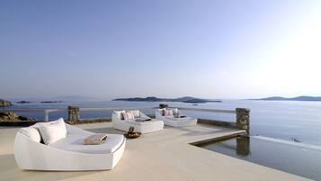 Una terrazza sul mare con sedute imbottite bianche e un parapetto in pietra che si affaccia su acque calme.