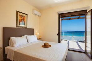 Ein Hotelzimmer mit Bett, einem gerahmten Bild an der Wand, einer Klimaanlage, einem Nachttisch mit Lampe und einem Balkon mit Meerblick.