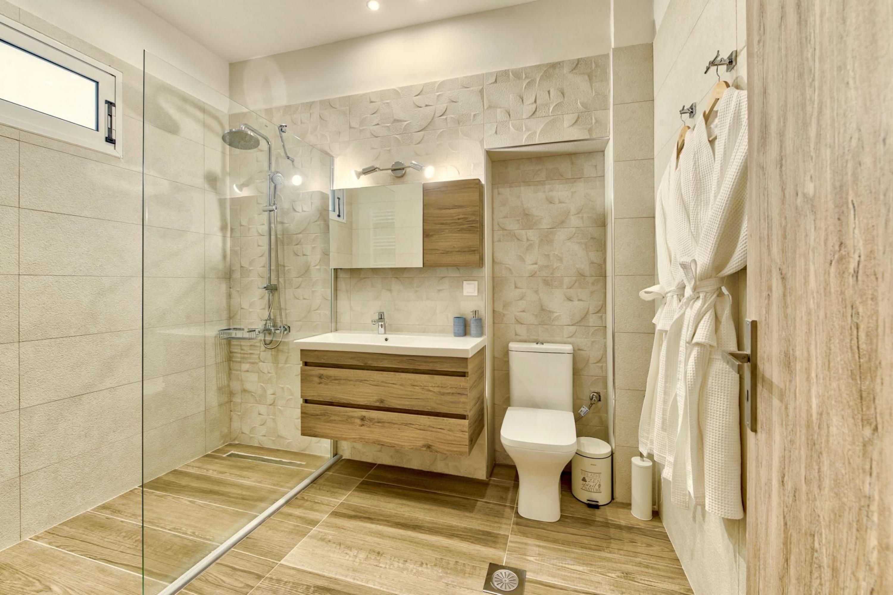 Une salle de bain moderne avec une douche à parois de verre, un meuble-lavabo en bois, des toilettes et un porte-serviettes.