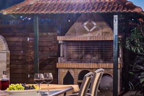 Un'area pranzo all'aperto con un tavolo di legno rustico, due bicchieri da vino e un piatto di uva.