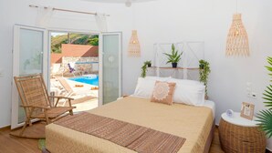 A bedroom with a bed, a chair, a bedside table, a lamp, and a view of an outdoor pool area. - Sky Beachfront Villa with private pool (Prinos)