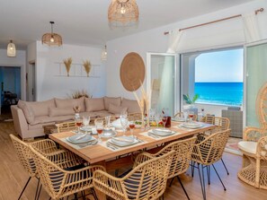 A dining area with a wooden table set for six, surrounded by wicker chairs, a beige sofa, and a view of the sea through a large window. - Sky Beachfront Villa with private pool (Prinos)