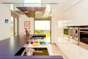 A modern kitchen with a built-in stove, a large island with a sink, and a view of the outdoors. - Luxury Villa Stella with private swimming pool (Chania)