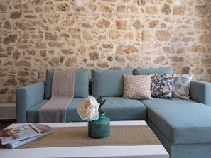 Ein Wohnzimmer mit Steinwand, einem türkisfarbenen Sofa, gemusterten Kissen, einer Vase mit Blumen und einer Zeitschrift auf einem Tisch.